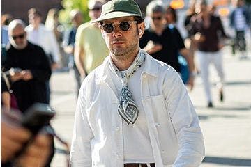 male model walking in the city wearing sunglasses, hat, scarf and overshirt