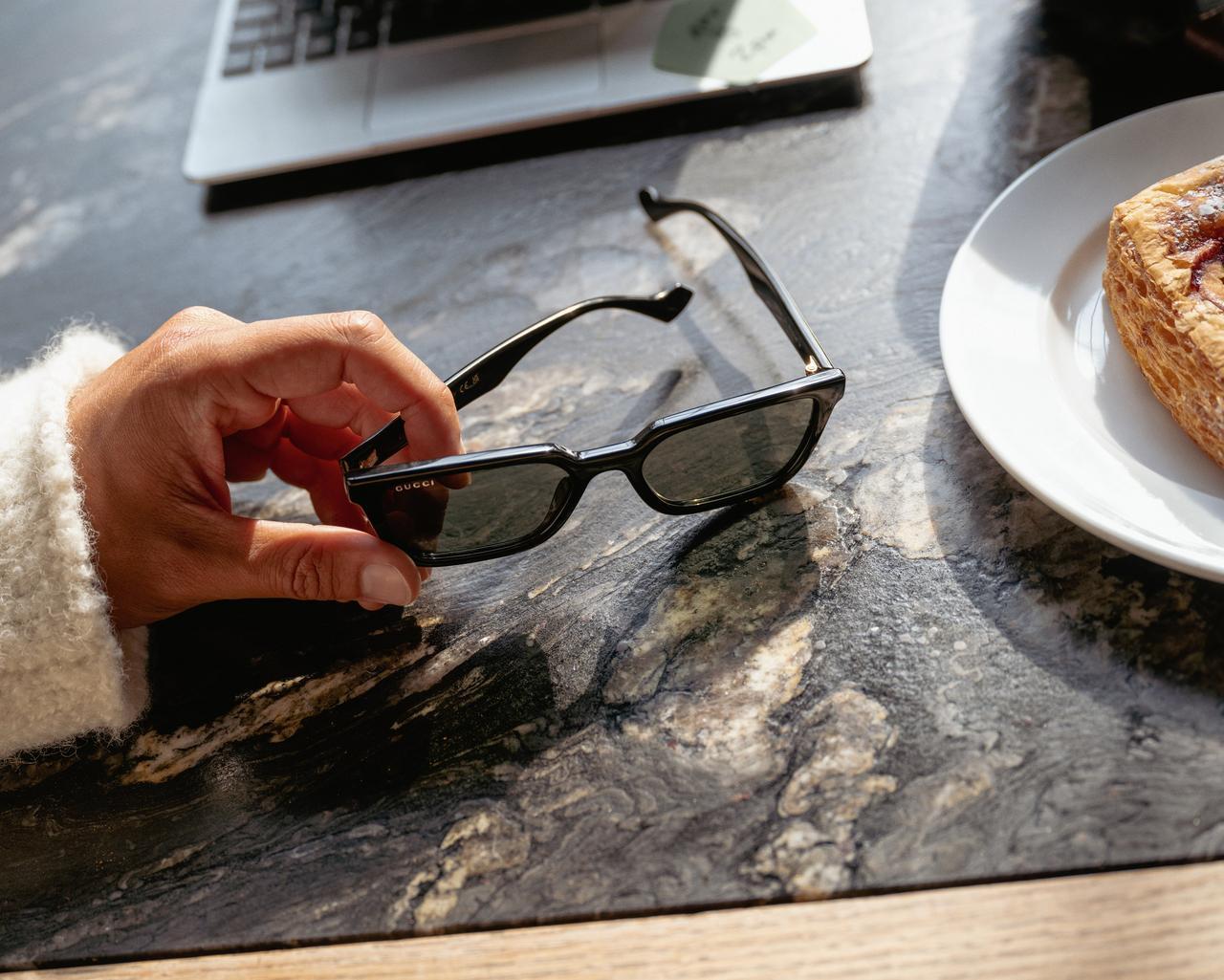 male hand holding sunglasses ontop of desk with laptop and food