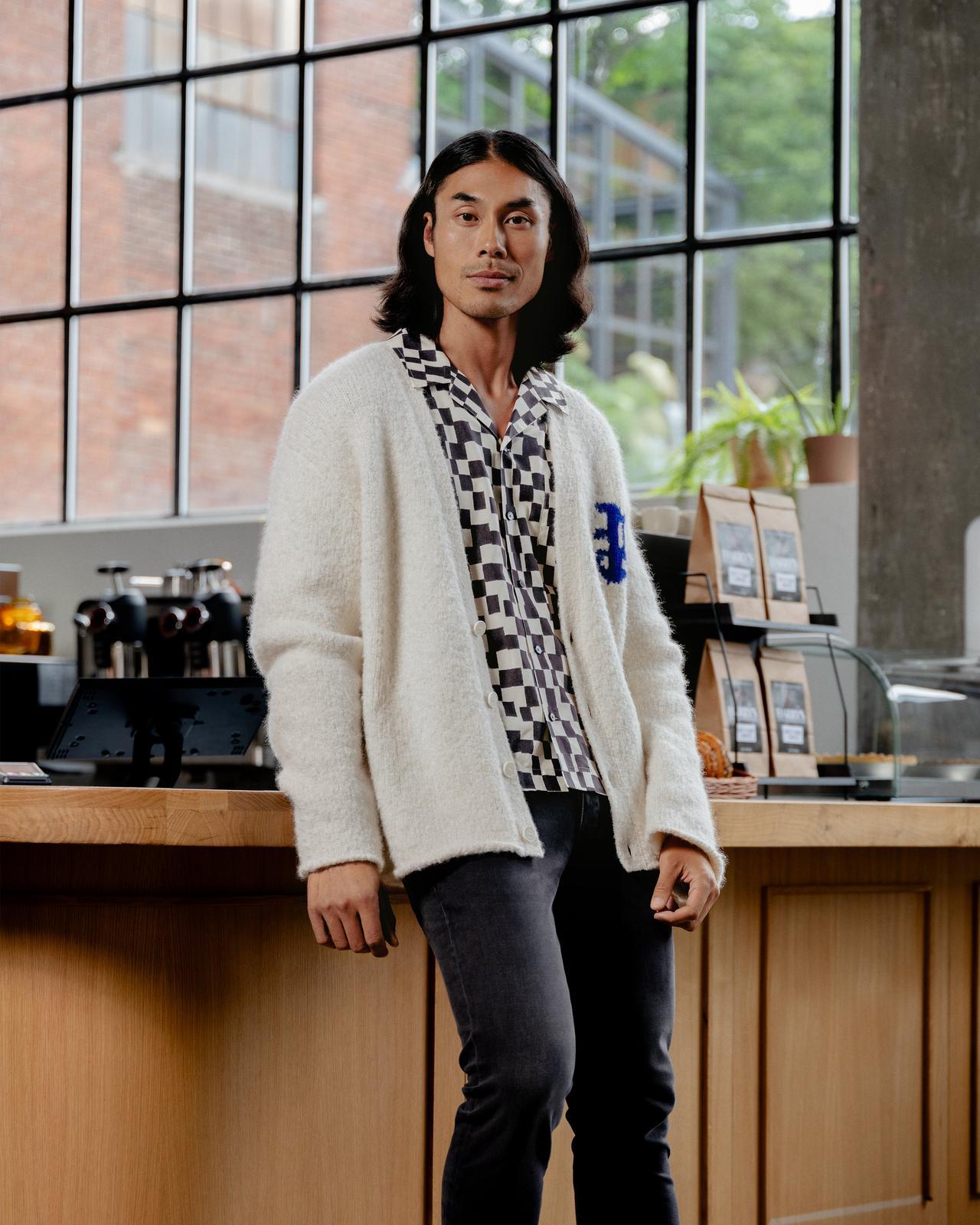 male model wearing cardigan and patterned dress shirt in cafe