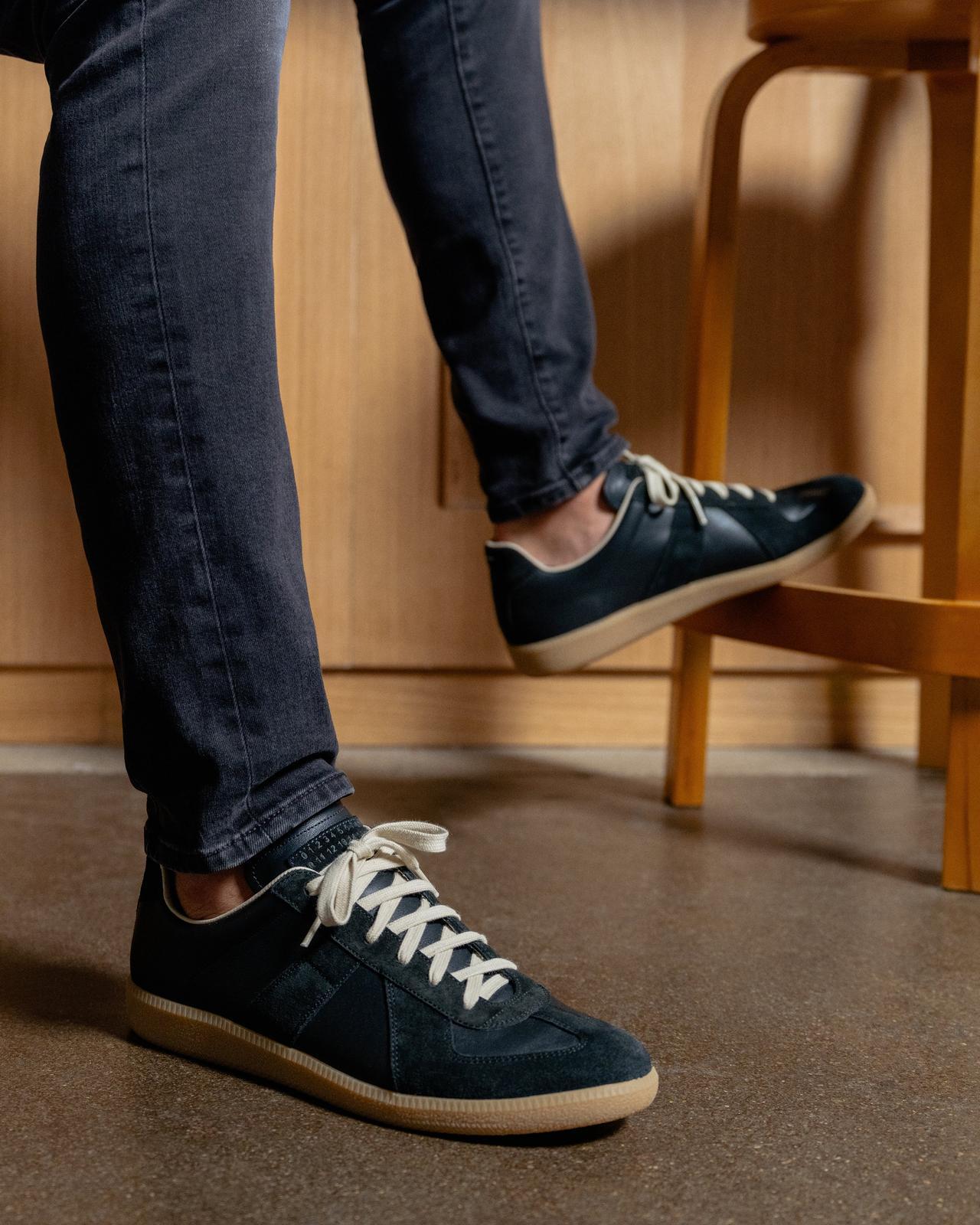 male model with one foot on stool wearing jeans and sneakers