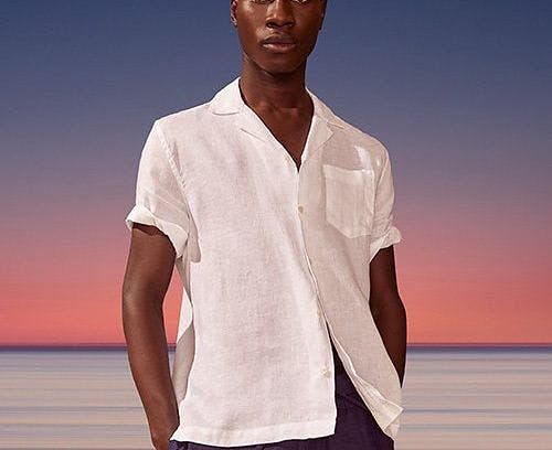 Un homme en chemise blanche debout sur une plage avec un coucher de soleil en arrière-plan
