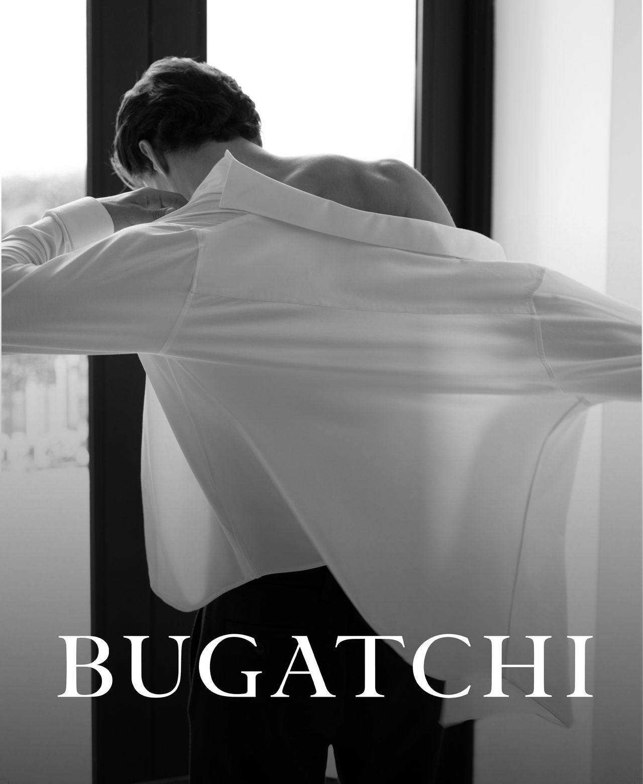 male facing window putting on bugatchi dress shirt
