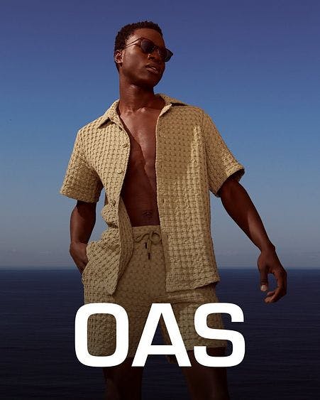 male model infront of ocean and blue sky with matching oas shirt and shorts