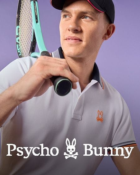 male model looking over shoulder holding tennis racket wearing psycho bunny baseball cap and polo