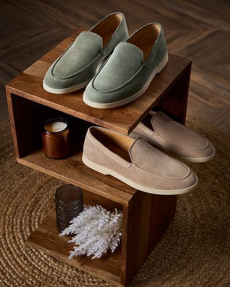 two pairs of loafers and two candles displayed on shelves ontop of carpet