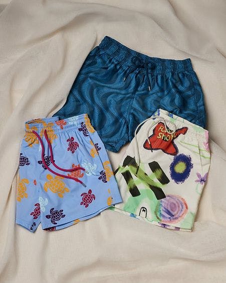 three pairs of colourfully patterned swimshorts on blanket