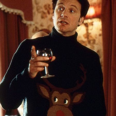 Colin Firth dans une scène de film : Discutant en pull de Noël moche vert foncé avec graphique de renne, tenant un verre de vin rouge