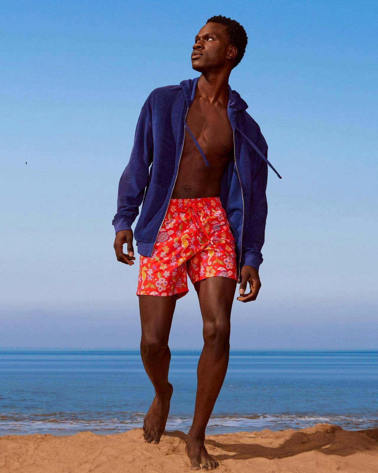 Un homme en veste bleue et en shorts sur la plage.