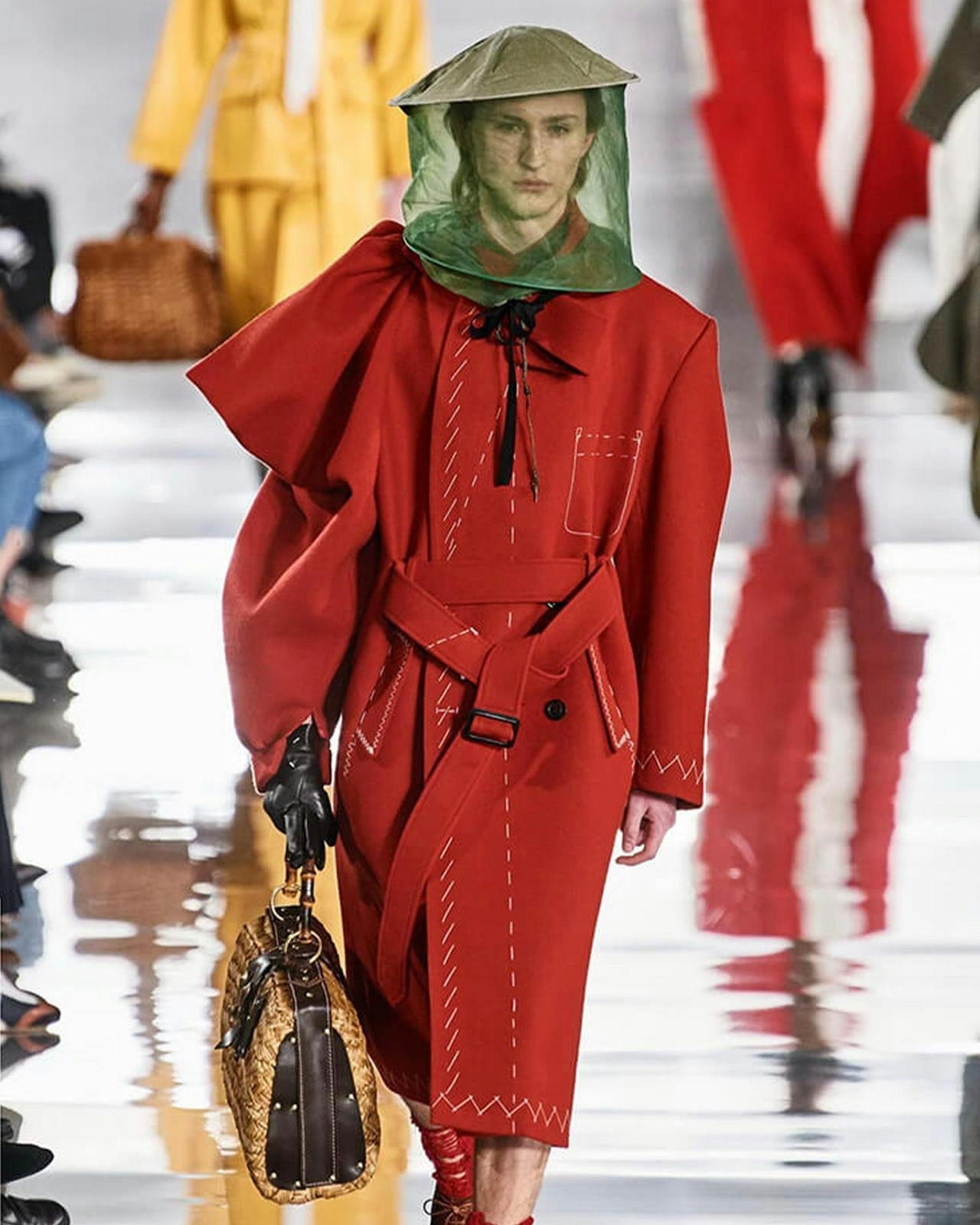 a model wearing a red coat with a bees nest hat