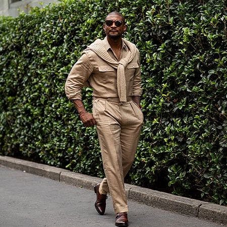 a man in a tan suit and sunglasses walking down a street