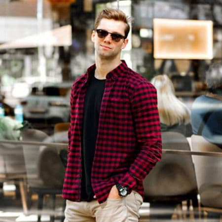 male model posing with one hand in pocket in the city wearing checkered sport shirt, t-shirt and jeans.