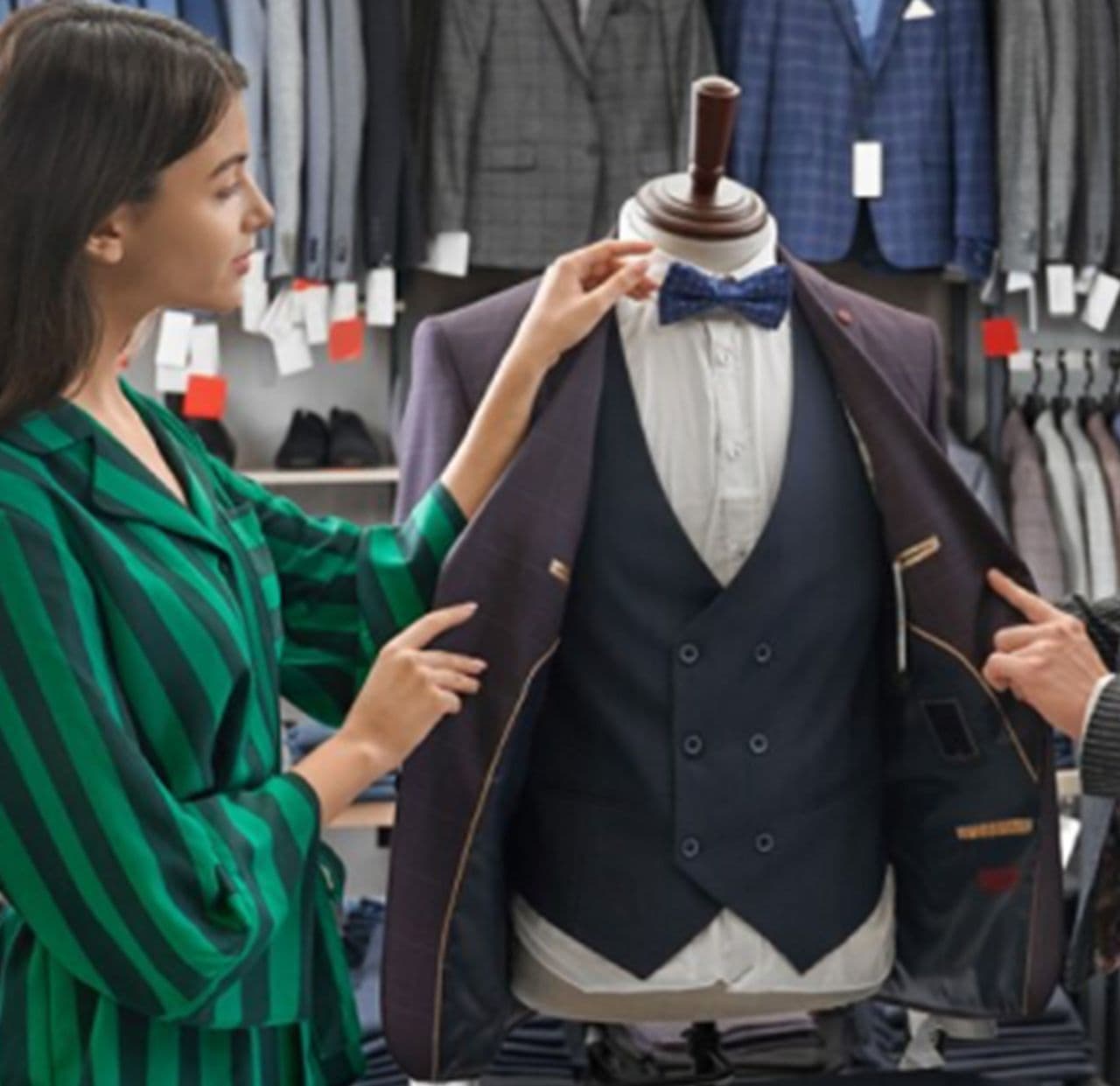 torso mannequin wearing dress shirt, vest and sport jacket while woman in harry rosen store adjusting bowtie on mannequin