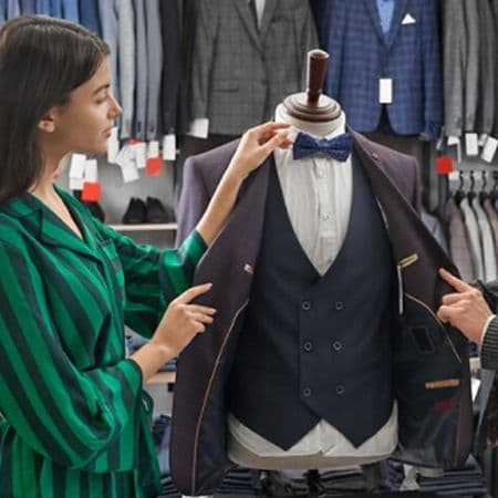 torso mannequin wearing dress shirt, vest and sport jacket while woman in harry rosen store adjusting bowtie on mannequin