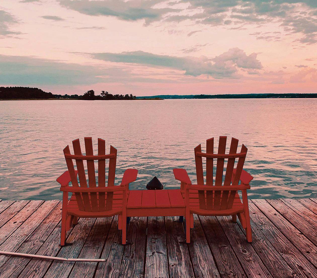 deux chaises de chalet classiques sur un quai en bois face au lac au coucher du soleil