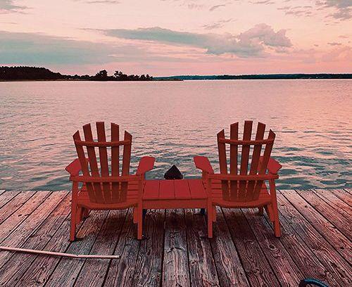 deux chaises de chalet classiques sur un quai en bois face au lac au coucher du soleil