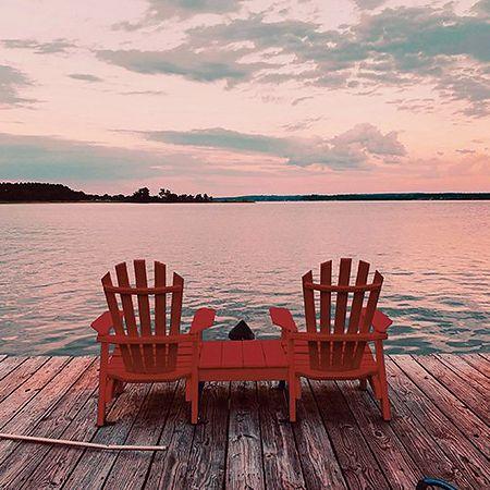 deux chaises de chalet classiques sur un quai en bois face au lac au coucher du soleil