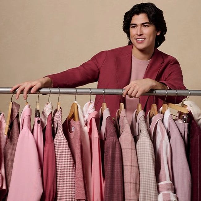 Un homme dans une veste rose souriant devant un portant à vêtements