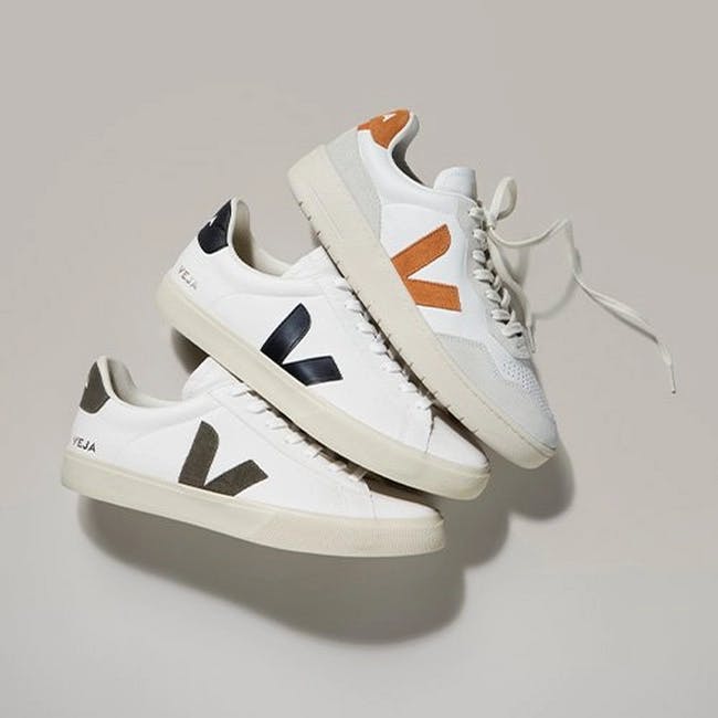 Three white VEJA sneakers with orange and black stripes on them