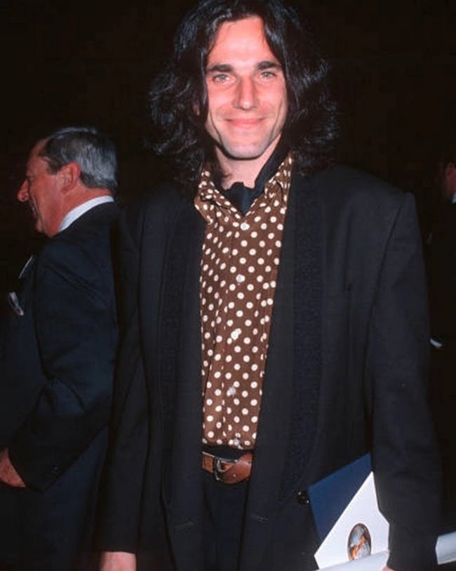 Daniel Day in a suit and tie holding a folder