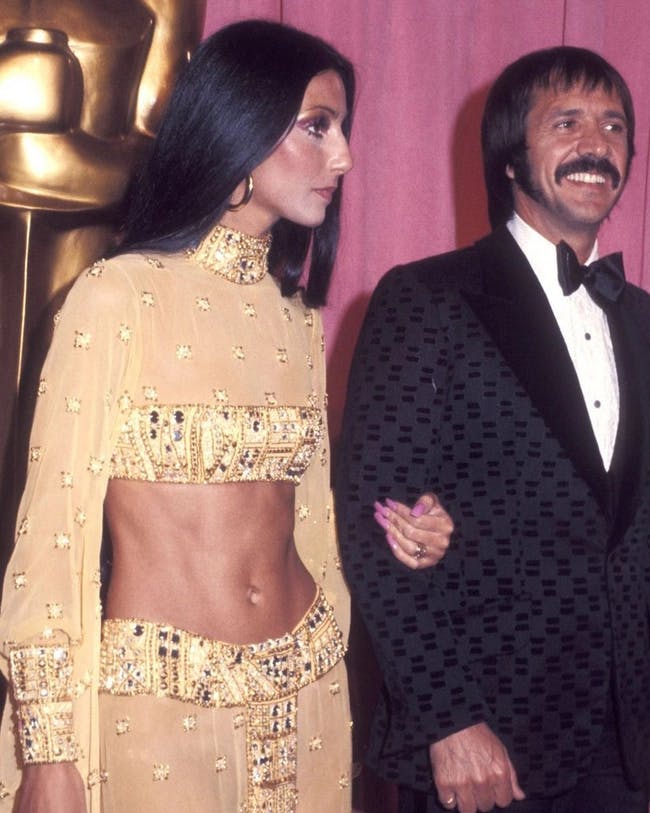 Sonny Bono and Cher standing next to each other in front of an oscar statue