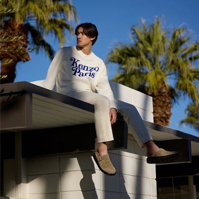 a man sitting on top of a building wearing a white kenzo sweatshirt